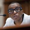A woman wearing glasses and a suit speaks into a small microphone as she sits in a congressional hearing room.