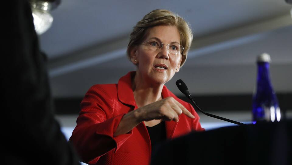 The senator gestures from a podium while in a red blazer.