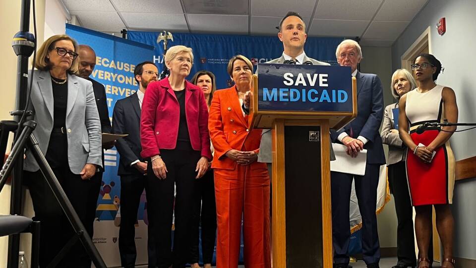 People gather around a podium bearing a sign that says "Save Medicaid."