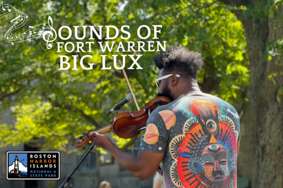 This is a photograph of a violinist who goes by the name 'Big Lux." We see him from the back, playing his violin. He is outdoors, surrounded by leafy trees and sunshine. Above him and to the left are the following words, written in white: "Sounds of Fort Warren, Big Lux."