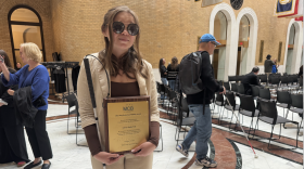 A woman wearing sunglasses holds a white and a bronze plaque.
