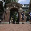 A handful of people who appear to be parents and students walk on the brick sidewalk on the edge of Harvard's campus.