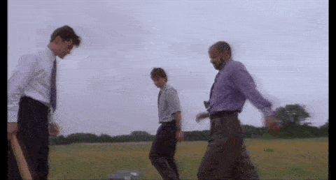 Three office workers destroy a printer in a field with their feet and a baseball bat