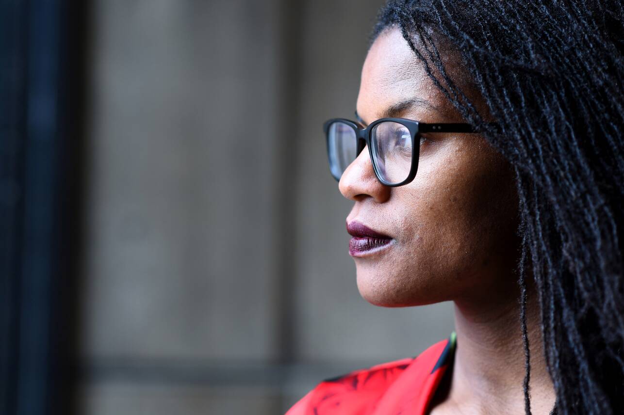 A portrait of a young Black woman wearing glasses and a red shirt looking off camera.