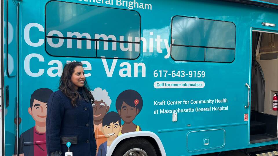 A woman smiles and stands outside a blue "Community Care Van" that offers mobile health services.