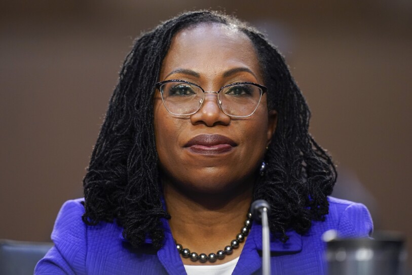 Ketanji Brown Jackson, a woman with glasses and braids wearing a blue blazer, white shirt and black pearl necklace, facing the camera.