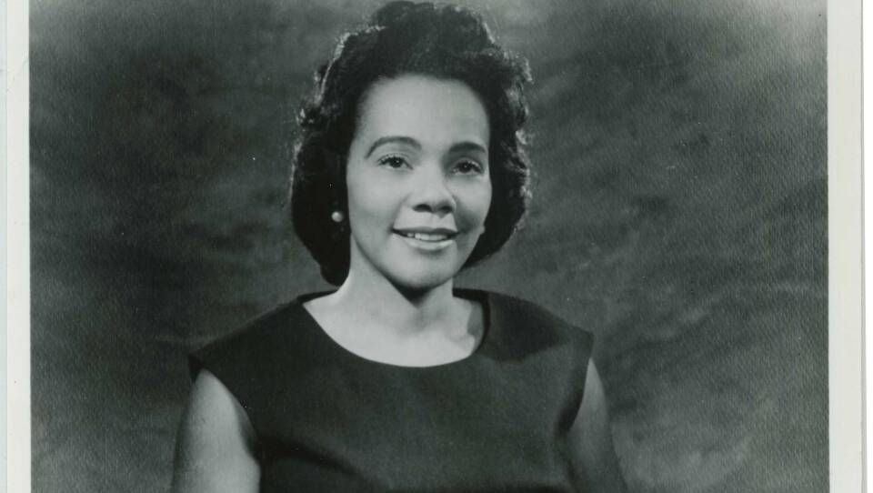 A young woman smiles for the camera in a posed school photo, wearing pearl earrings and a black dress.