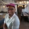 Williams sits in an empty restaurant, smiling at the camera.