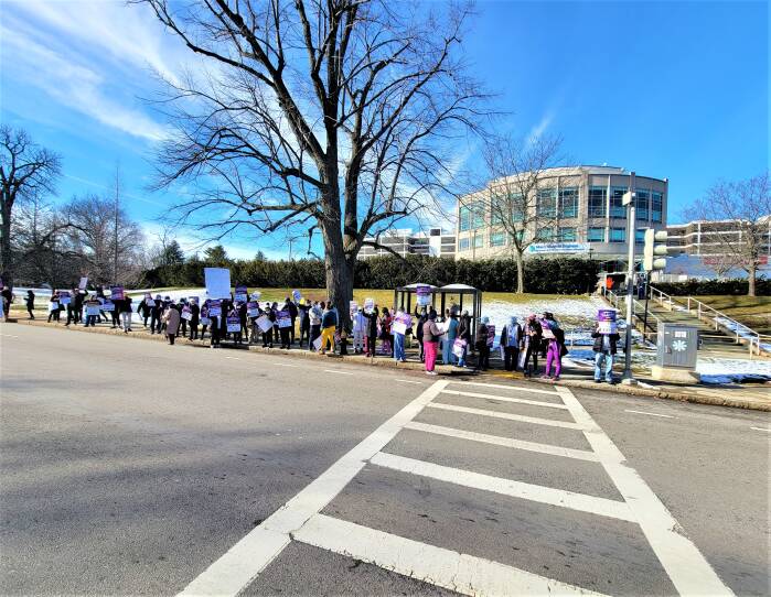 People holding signs line the sidewalk outside a hospital building on a winter day.