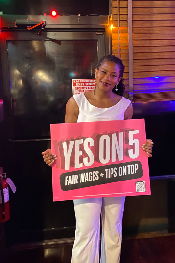 A woman dressed in white holds up a "Yes on 5" sign.