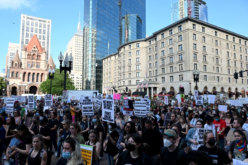 Hundreds of protestors holding signs stand in Boston.