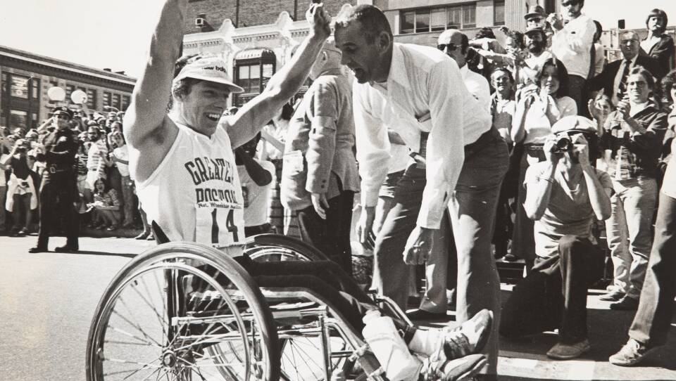 Black and white image of a man in a wheelchair crossing the finish line at the Boston Marathon