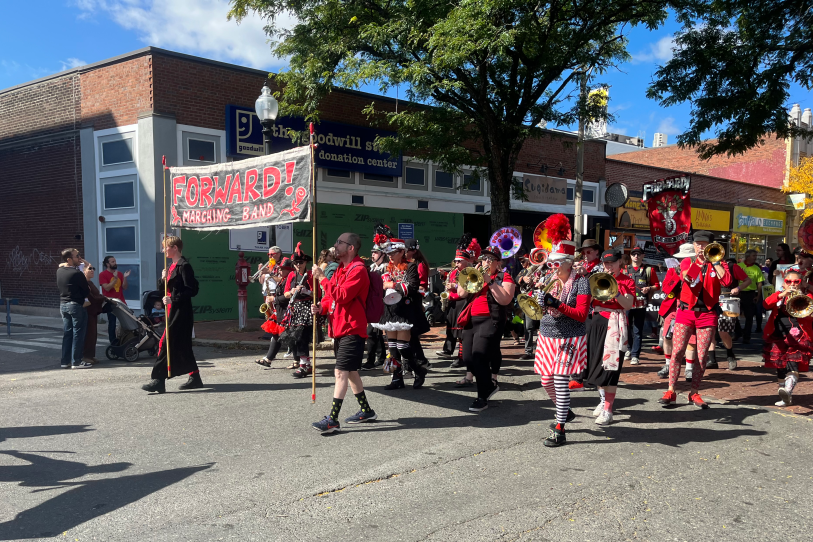Dozens of people in bright red outfits walk through streets with their brass instruments.