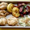 Six fried dumplings of different varieties are on a small metal tray next to a salad of roasted carrots and delicata squash and a cabbage slaw.
