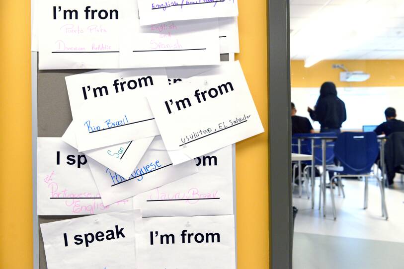 On a yellow wall outside a classroom, a number of signs hang, reading "I'm from Rio, Brazil," "I'm from El Salvador," "I speak Portuguese and English" and "I'm from Dominican Republic."