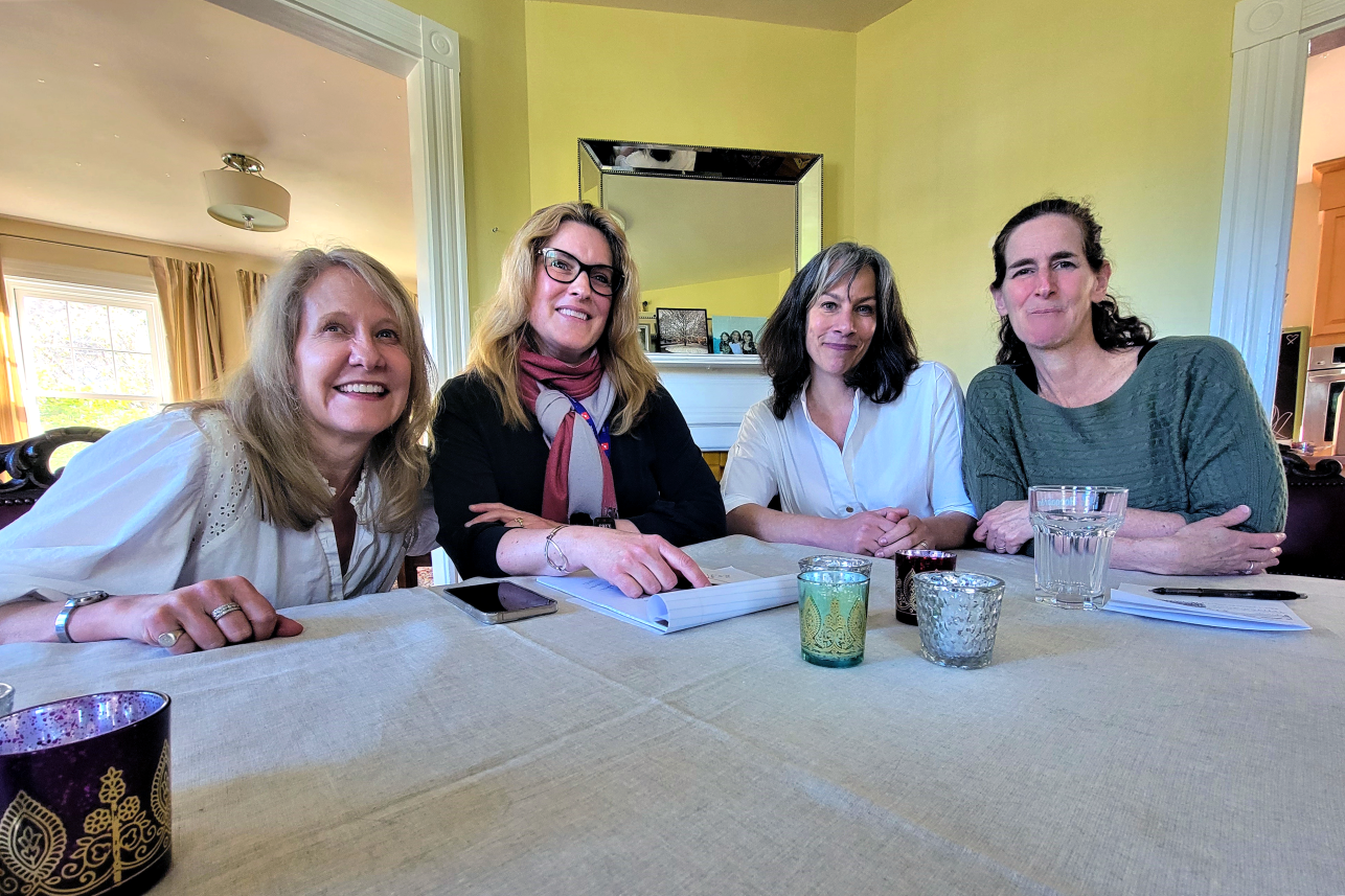 Four women sit at a kitchen table, smiling for the camera.