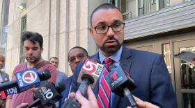 A man in a suit and striped tie speaks into one of many local reporters' microphones