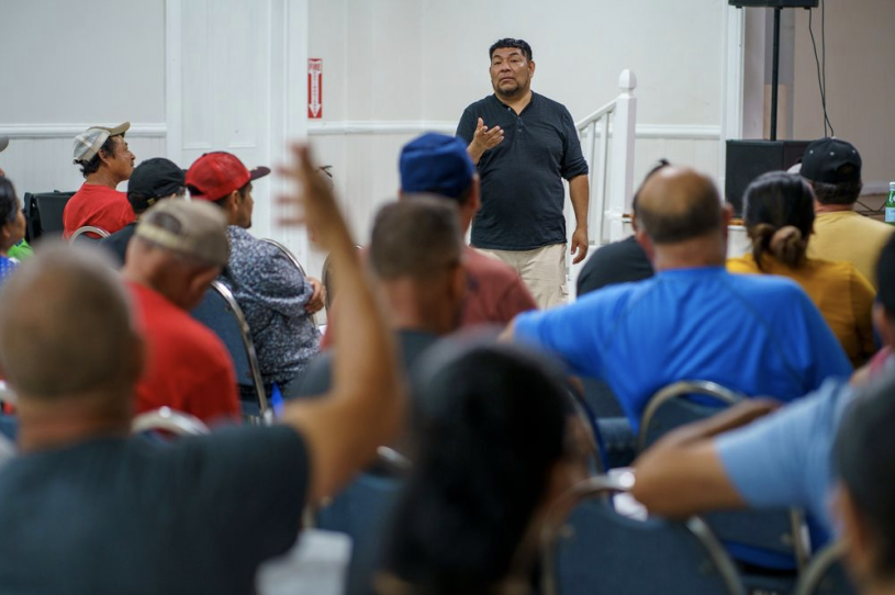 A man stands in front of dozens of people in chairs who are asking him questions