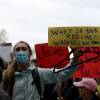 A woman wearing a mask holds a coat hanger and handwritten sign reading "What is your red line? When will you show up?"