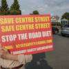 A man holds a red sign with the words "save Centre Street, safe Centre Street, stop the road diet."