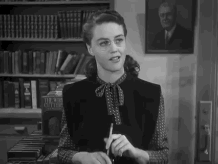 Actress Dorothy Malone stands in a bookstore. She looks at someone off camera and leans back, making an impressed face.