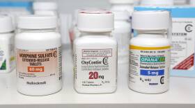 Bottles of morphine, OxyContin, and other opioids are lined up on a shelf.