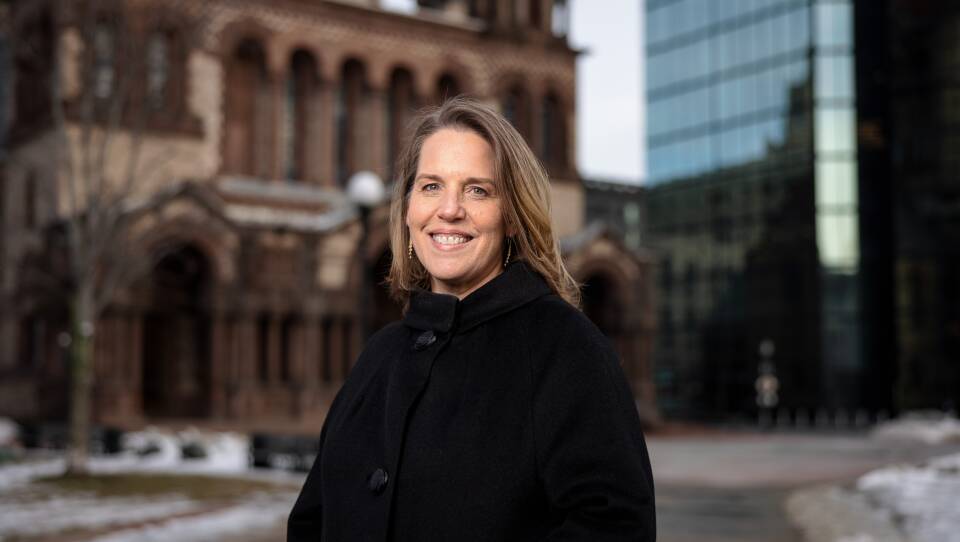 Gail poses in front of the old church in Copley Square, smiling at the camera wearing a black jacket