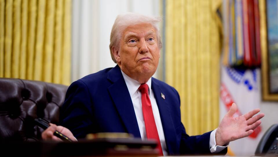 Donald Trump waves his hands as he sits behind his desk in the Oval Office.