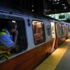 A subway train at night, with a conductor leaning out of a window speaking into an intercom.