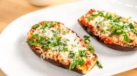 White oval plate with two eggplant halves topped with marinara sauce, cheese, and fresh basil