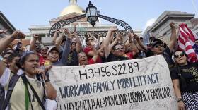 A crowd of dozens cheers and holds a sign bearing the words "Work and Family Mobility Act" alongside their signatures.