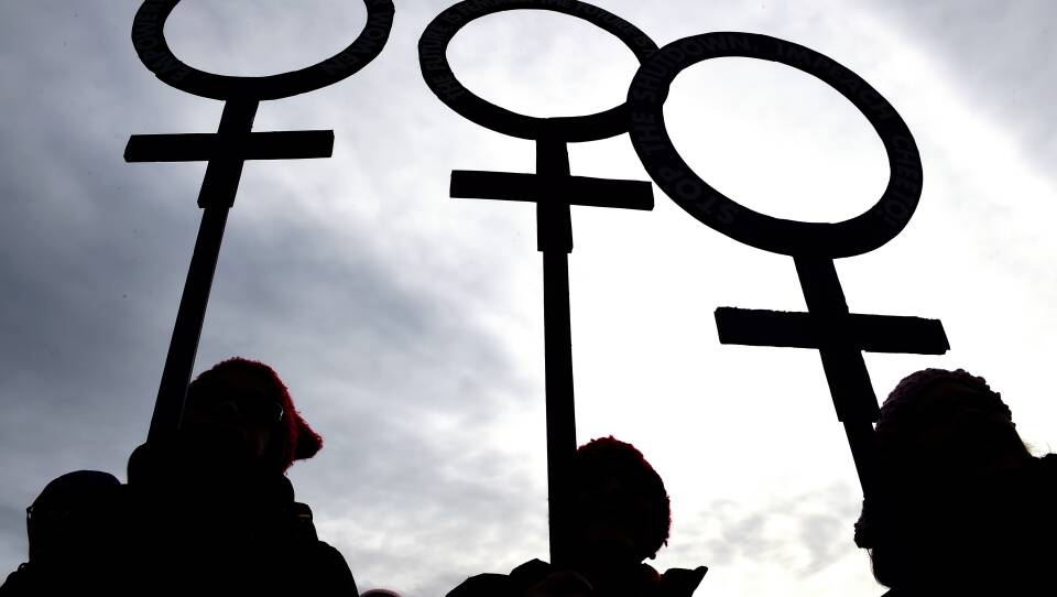 A silhouette photo of three people holding female symbol signs.
