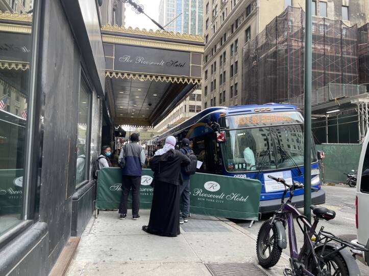 People deboard a bus just outside the entrance to a hotel.