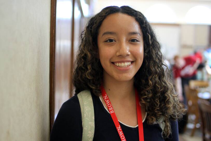 A young woman smiles for the camera, wearing a bright red lanyard that reads "BROWN".