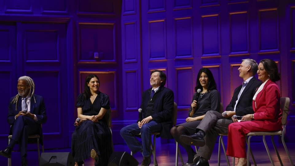 A group of six people seated on chairs on the stage at Symphony Hall (three men and three women).