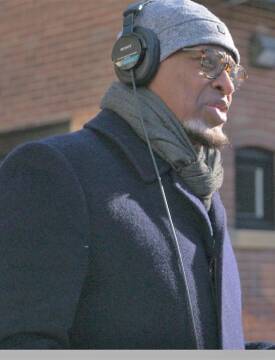 A man dressed in winter garb stands with a mic, interviewing a subject.