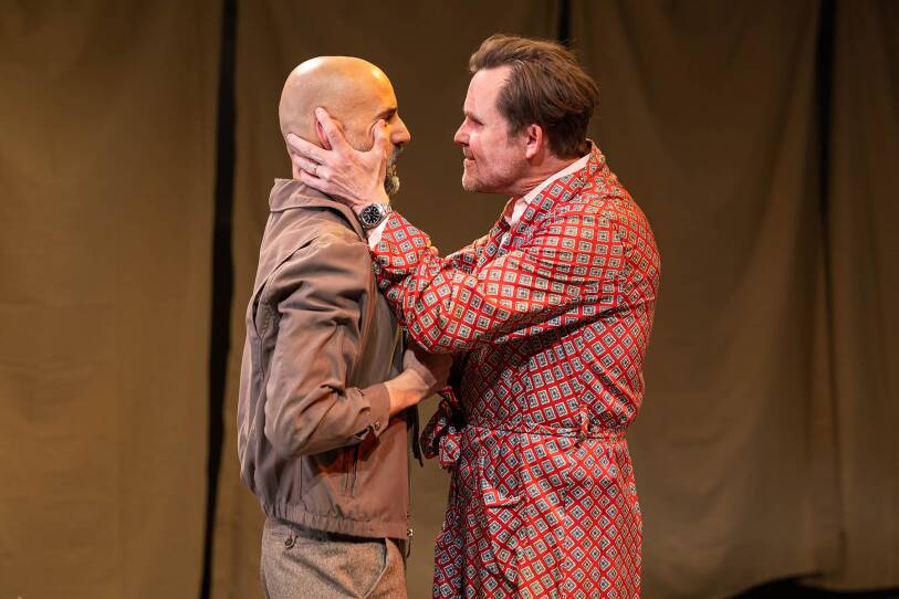 Two actors stand very closely, face-to-face. One man has the other man's face in his hands. They look to be in an emotionally charged moment