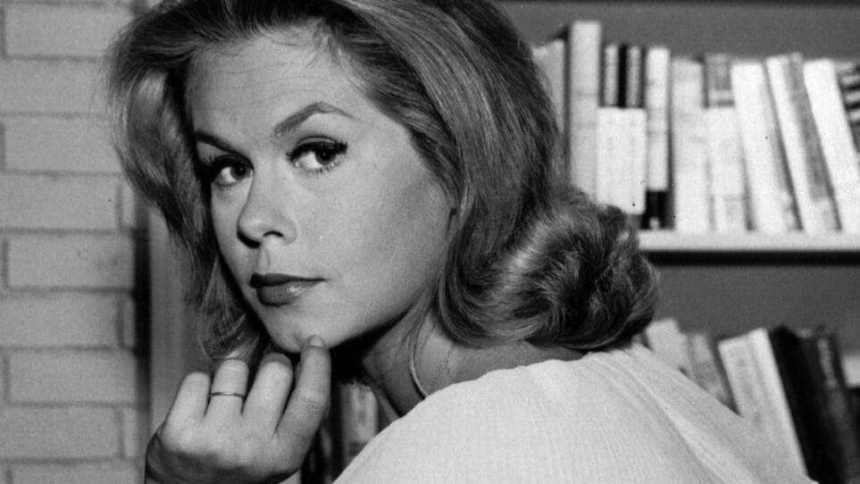 A black and white photo of a woman looking over her shoulder with her hand on her chin.