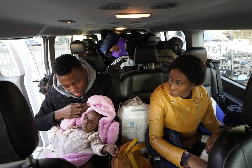 Inside a van, a father holds a baby in his lap while his wife looks at them.
