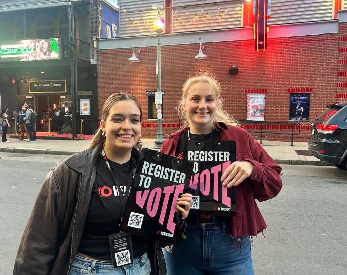 Two people wearing Headcount shirts holding clipboards with the words "register to vote."