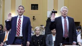 Two men in suits hold up their right hand in a room in the U.S. Capitol.
