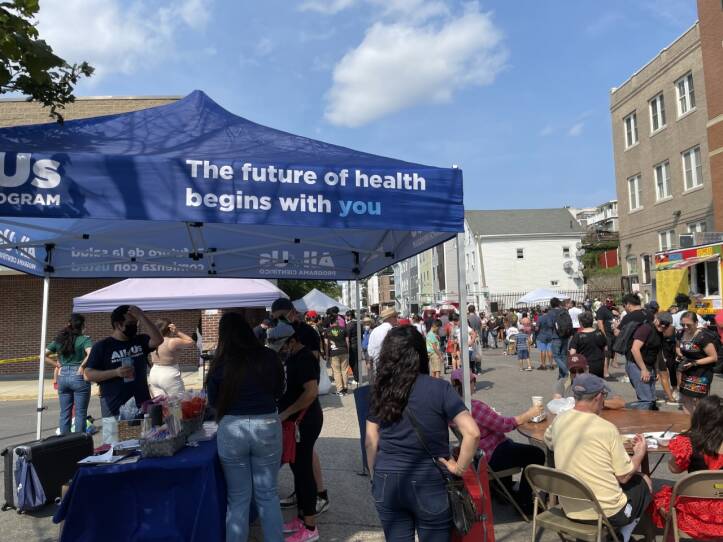 On a busy East Boston Street of pedestrians, volunteers stand under a blue tent