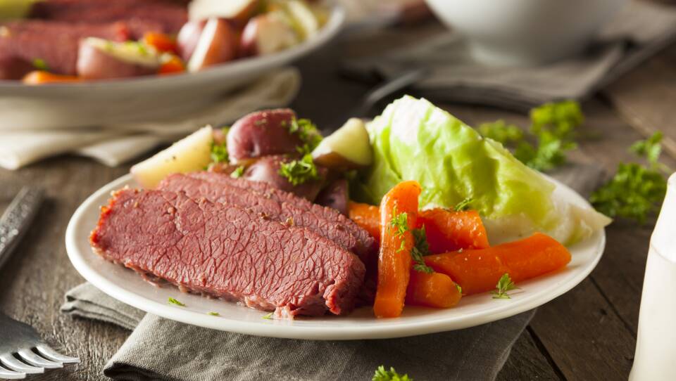 A plate has pices of corned beef, carrots, cabbage and potatoes.