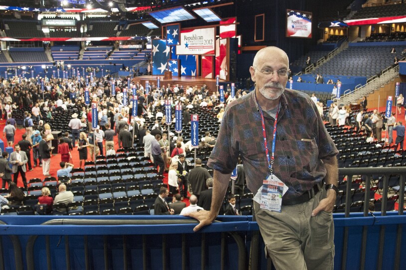 A man with a press badge in a large arena filled with delegates.