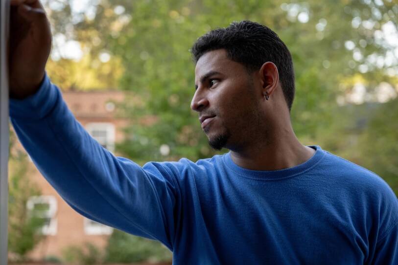 A man in a blue sweater leans against a doorframe.