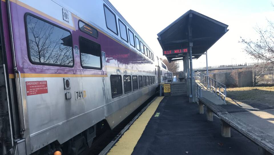 A silver and purple commuter rail train lines up next to an outdoor passenger station.