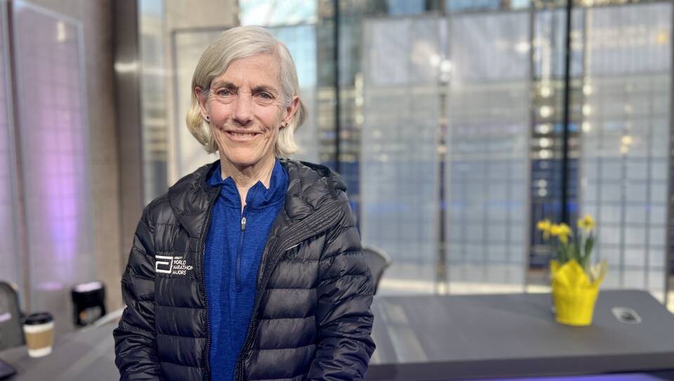 Joan Benoit stands inside a brightly lit studio, smiling.