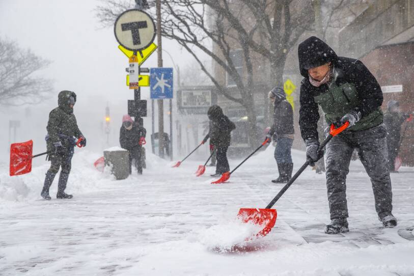 People shovel outside in a blustery snowstorm.