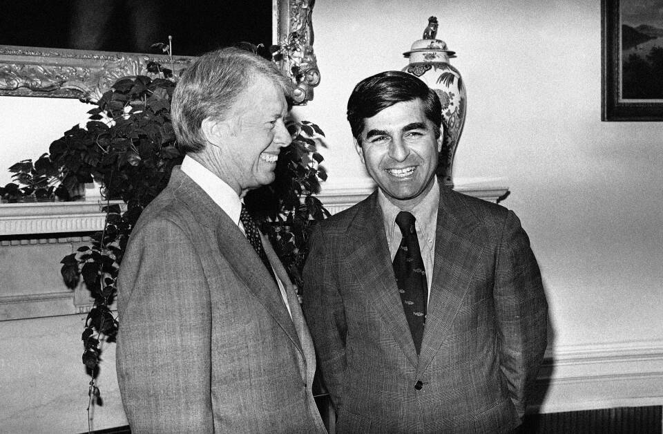 Jimmy Carter and Michael Dukakis smile as they talk in a room of the White House.
