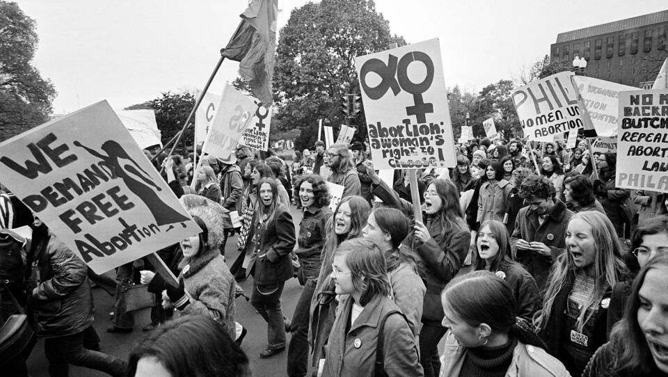 A black-and-white photograph of a large crowd marching and chanting as they hold signs in favor of abortion rights.